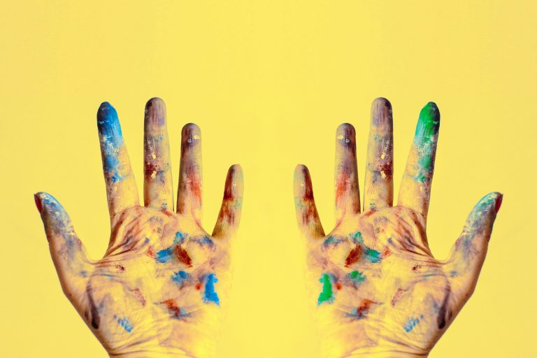 Colorful fingers spread against a bright yellow backdrop, showcasing creativity.